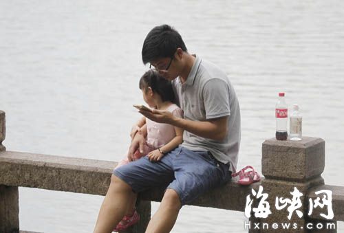 前日，西湖公园柳堤边，一位爸爸搂着女儿坐在湖边，女儿望着远处的游船，而爸爸一直盯着手机