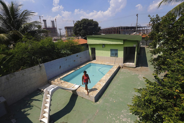 当地时间2016年1月28日，巴西里约，57岁的Marcia Lemos站在自家院子的游泳池边，后方正在进行奥林匹克工程的建设。