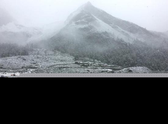 9月20日，受冷空气影响，四川甘孜州稻城亚丁景区雪花飘舞，大雾弥漫，山峰披上白纱，银装素裹。正在景区内游玩的海内外游客纷纷用手机记录雪景，并拍照留念。钟欣 摄